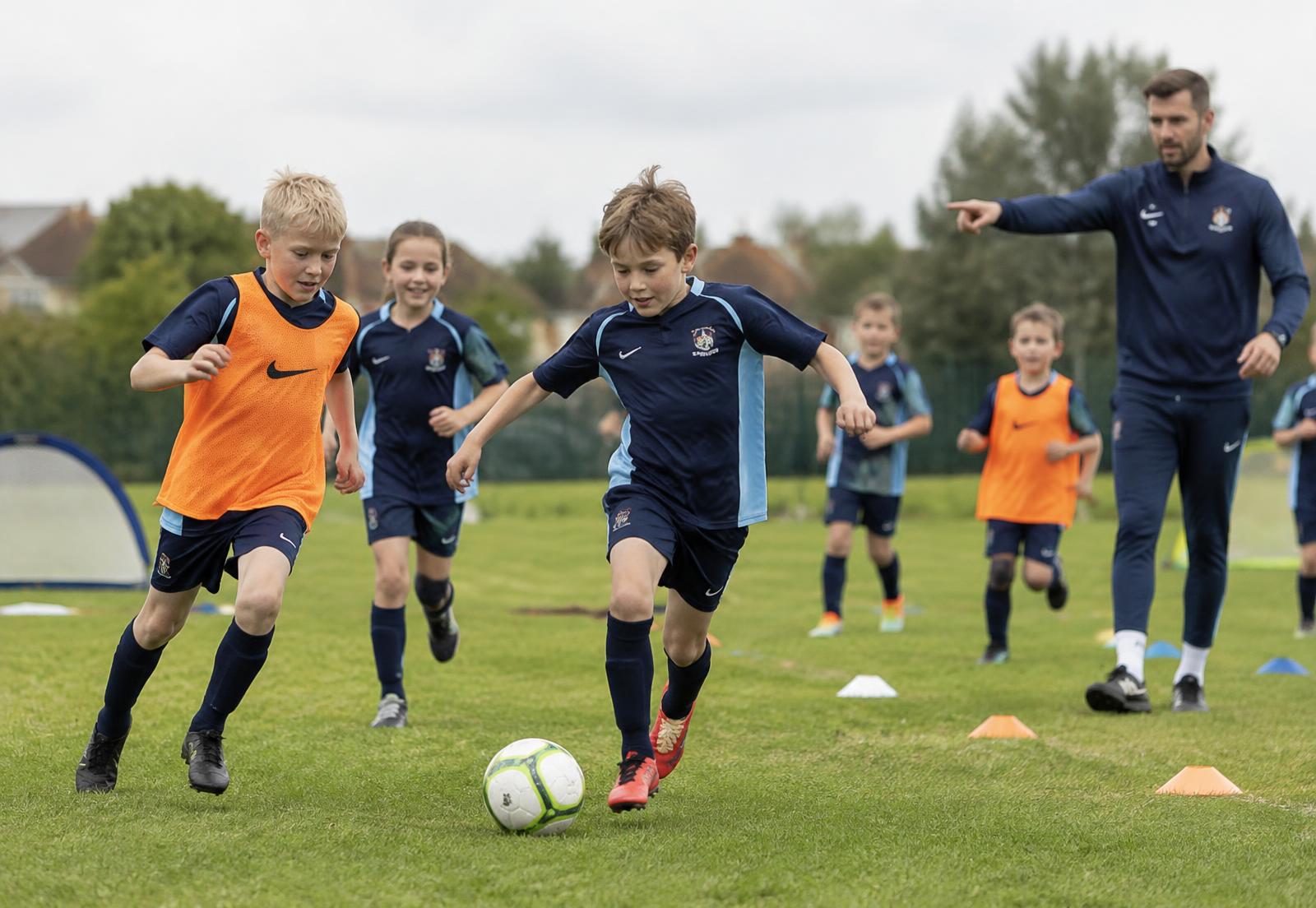 Primary school children in sports kit playing football with an ETT Sports coach on a school field